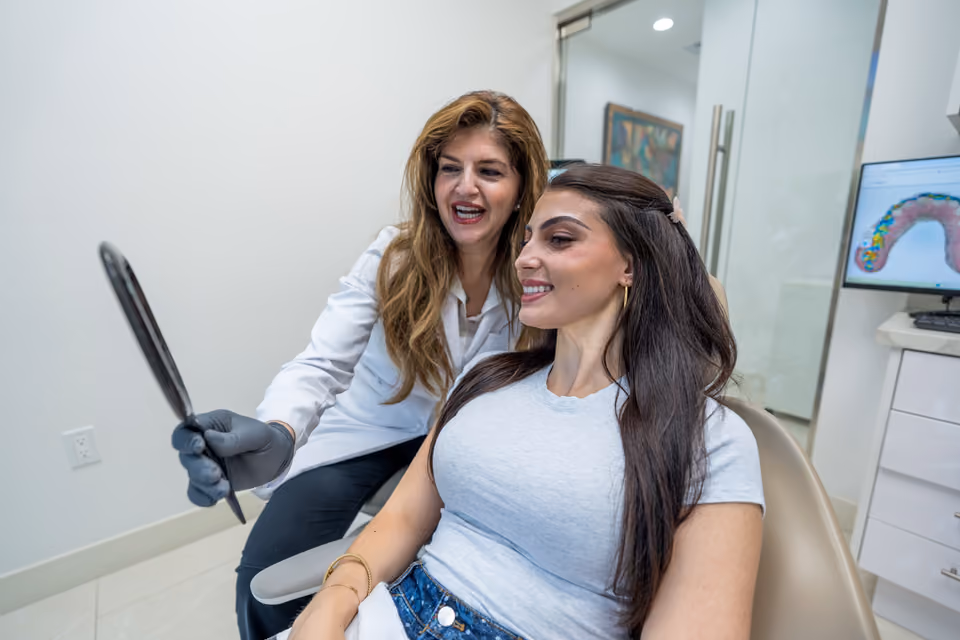 A dentist and patient check her smile in a hand mirror.