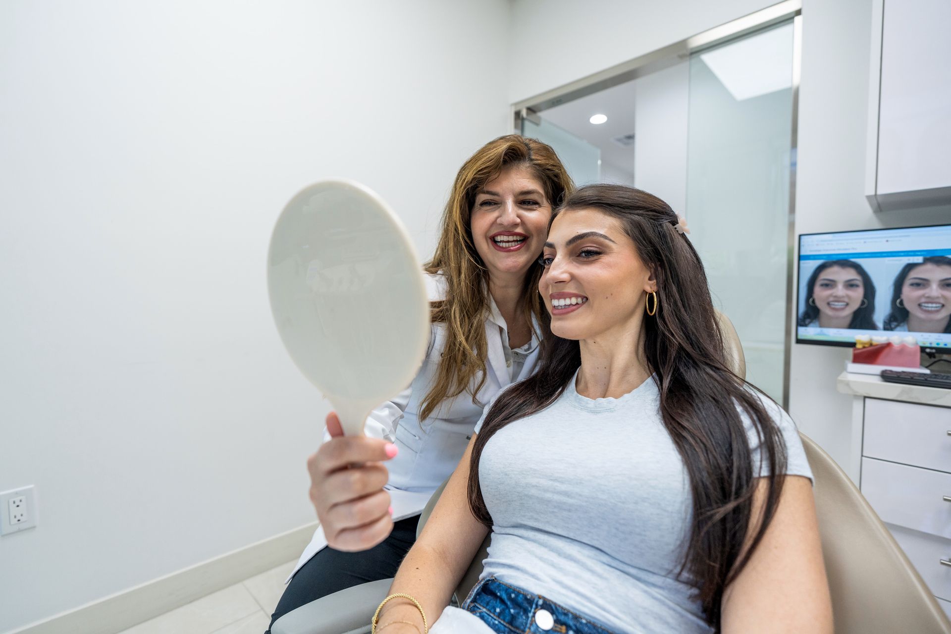 A smiling patient admires her smile in a hand mirror beside her dentist at Aliso Creek Dental.