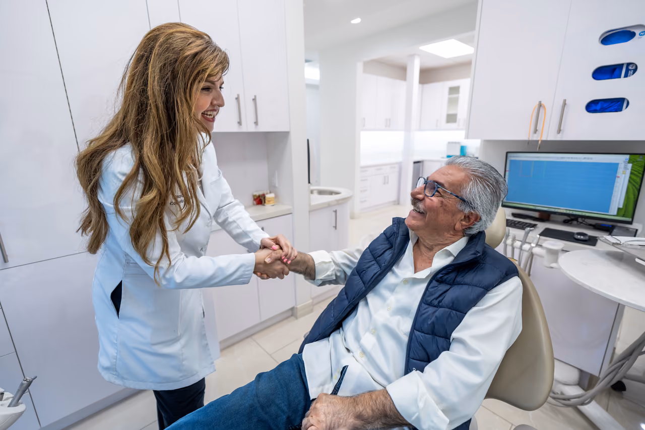 A dentist warmly greets a patient in the treatment room.